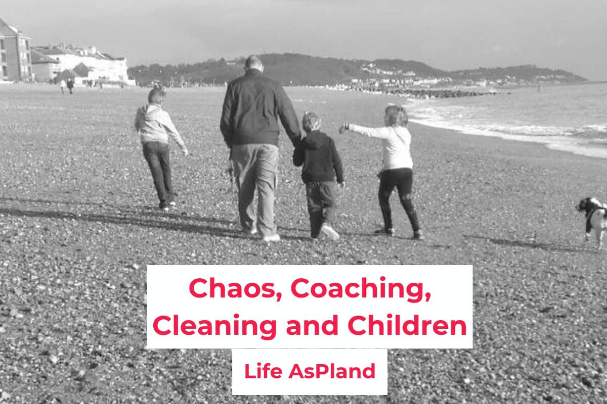 Three young children walking on the beach with their father, walking away from the camera