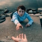 Woman reaching out to grab someone's hand as she climbs up a wall