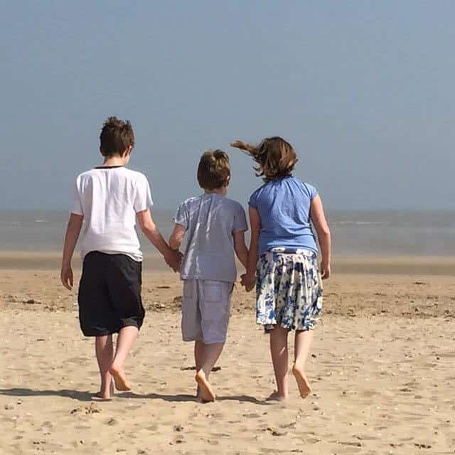 Three young children - a girl and two boys - walking hand in hand along a beach